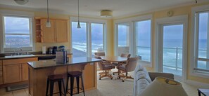 Een keuken met een groot schiereiland, barstoelen en uitzicht op de oceaan door grote ramen.
