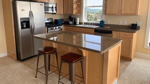 Une cuisine moderne avec des meubles en bois, des appareils en acier inoxydable, un grand îlot central avec des tabourets et une fenêtre offrant une belle vue.
