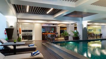 A modern indoor pool area with lounge seating, a bar, and a dining area.