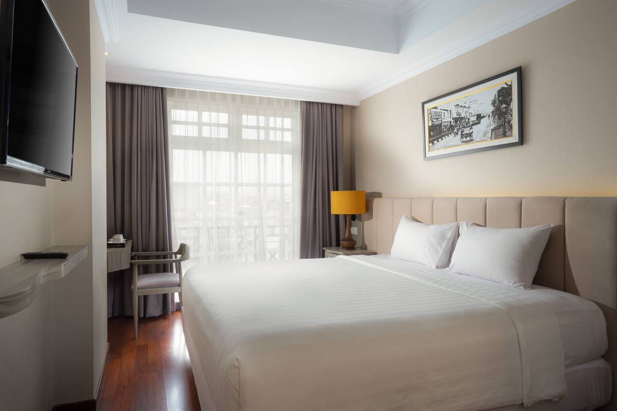 Une chambre d’hôtel avec un grand lit, un bureau avec une chaise, une télévision et une fenêtre avec des rideaux.