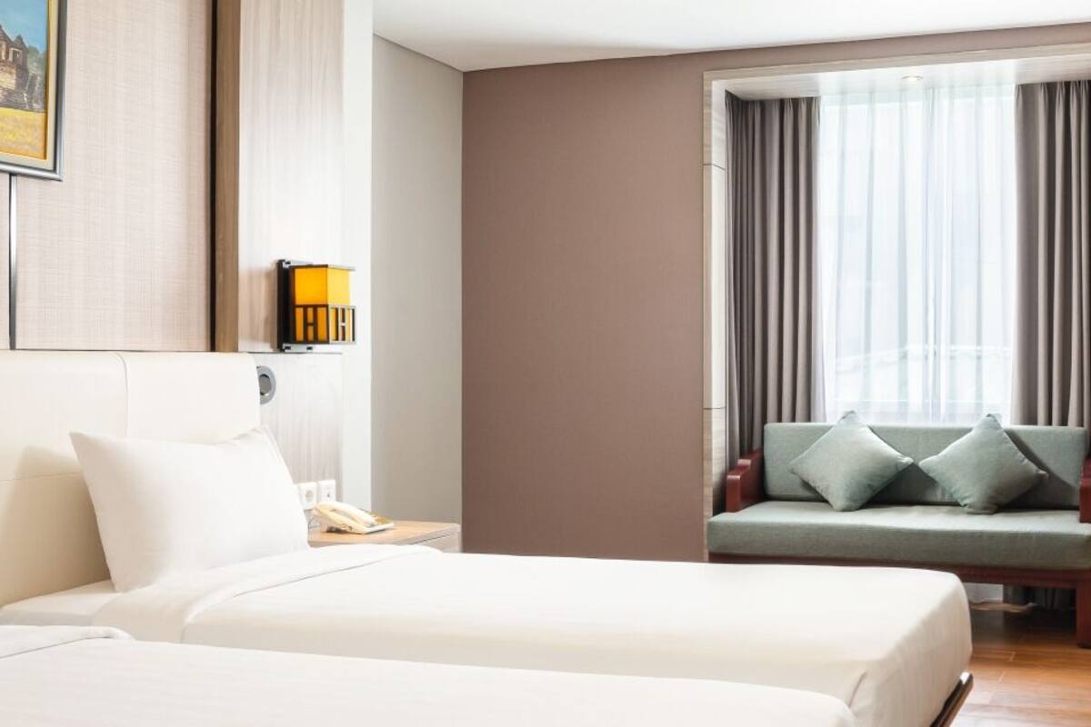 Une chambre d’hôtel avec deux lits, un bureau, une chaise, une télévision et une fenêtre avec des rideaux.