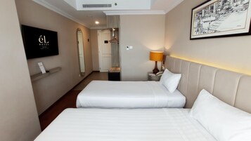 A hotel room with two beds, a TV, a framed picture, and a lamp.