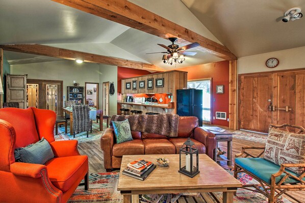 A spacious living room with a wooden ceiling, a brown leather sofa, a red armchair, and a wooden coffee table with books and a candle.