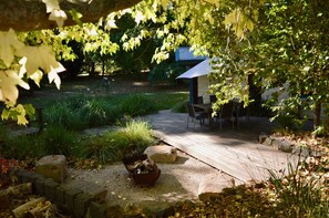 Step into a serene garden oasis with a wooden deck leading to a covered seating area surrounded by lush plants and a stone pathway.