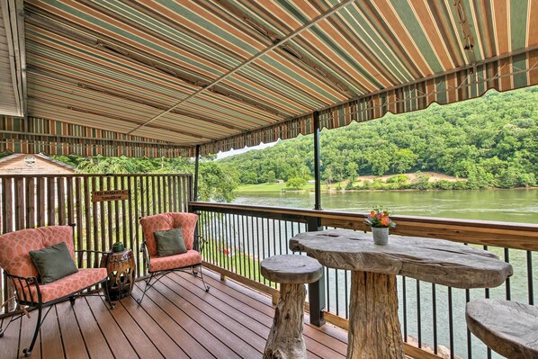 Una terraza techada con mobiliario de madera y vistas a un lago y un bosque.
