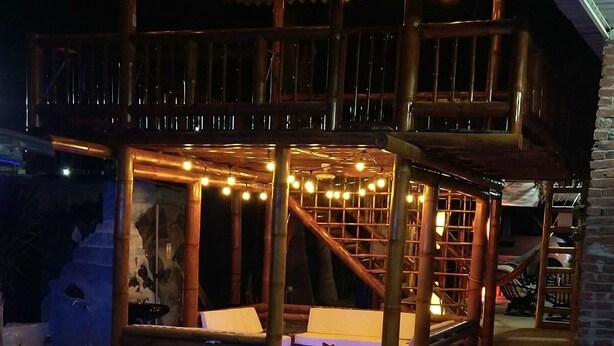 A covered outdoor seating area with string lights, a pool with blue lighting, and a bamboo structure. - Soga Hostal (Santa Marianita)