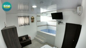 A hotel room with a bed, a small sofa, a TV, a window with curtains, a bathtub, and a door. - Soga Hostal (Santa Marianita)