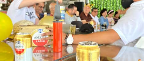 Zona de bar con personas sentadas en mesas, algunas sosteniendo bebidas.