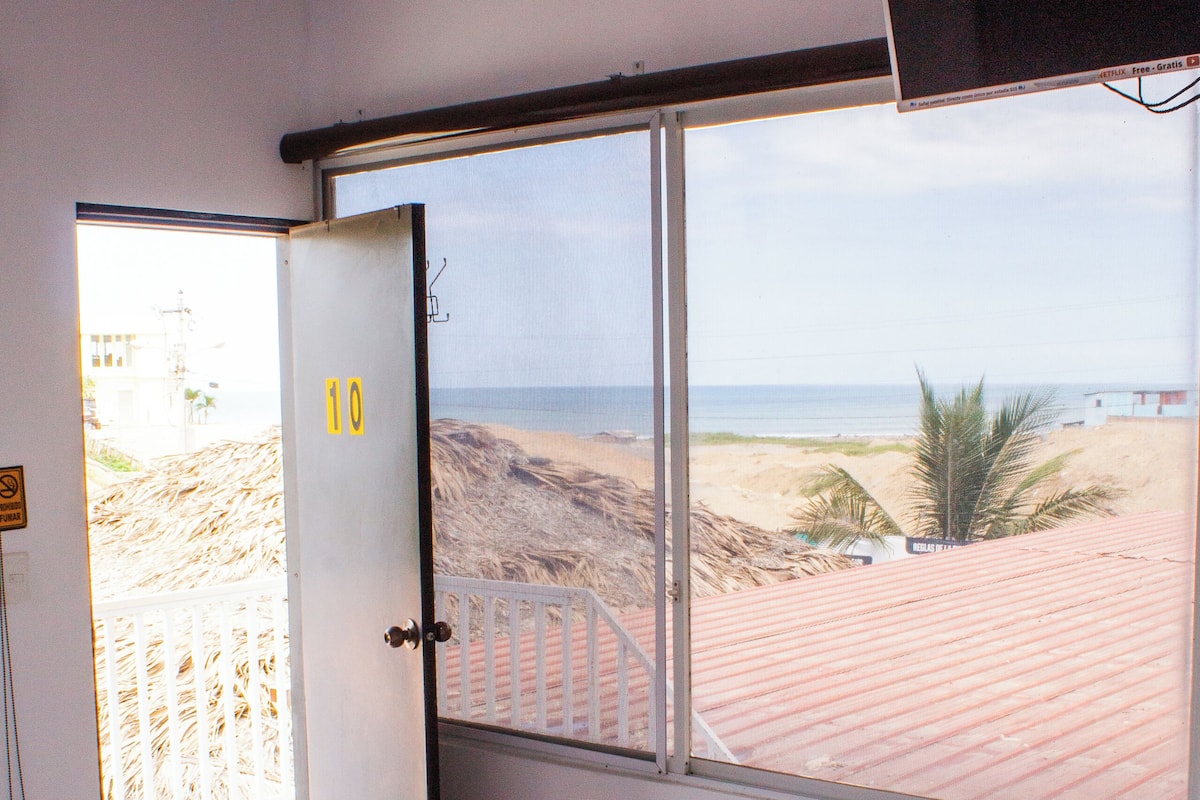 A hotel room with two beds, a large window with a beach view, and a TV mounted on the wall.