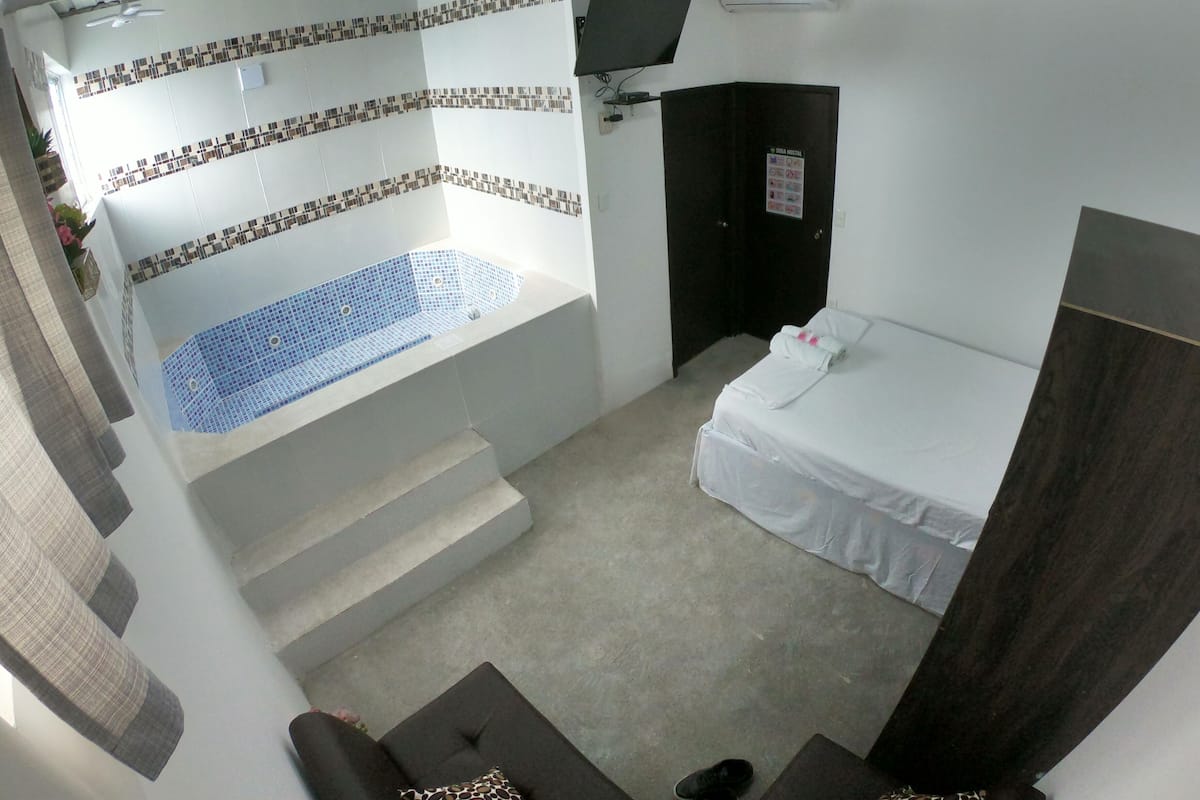A small, compact room with a single bed, a small seating area, and a bathtub with mosaic tiles.
