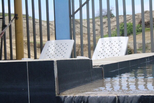 Zona de piscina amb dues gandules blanques, una paret blava i un paisatge sorrenc al fons.