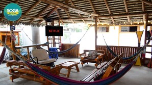 A hammock lounge area with wooden furniture, a sign indicating a Netflix service, and a thatched roof structure. - Soga Hostal (Santa Marianita)