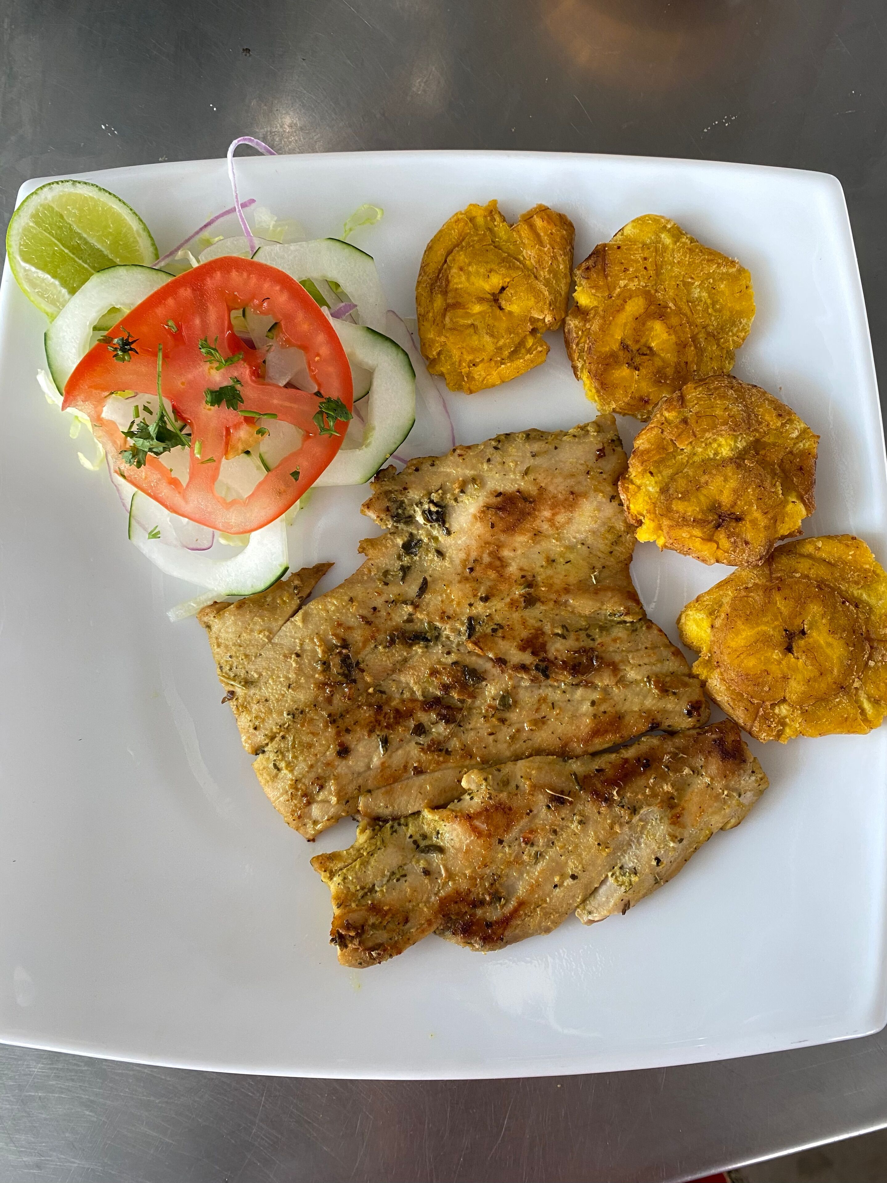 Une assiette composée de viande grillée, de bananes plantains frites et d’une salade fraîche.