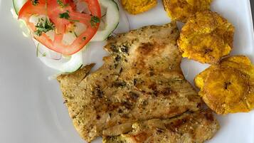Une assiette composée de viande grillée, de bananes plantains frites et d’une salade fraîche.