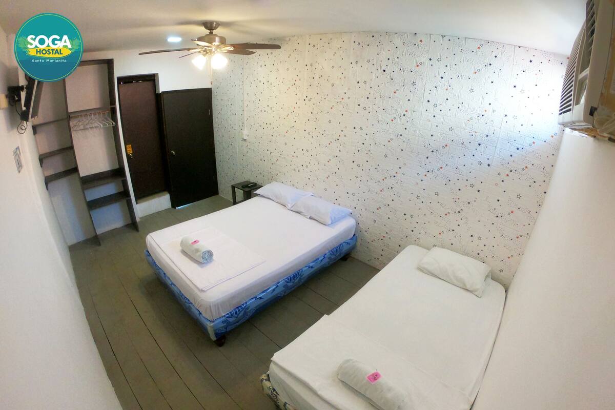 A room with two beds, a ceiling fan, a patterned wall, and a door.