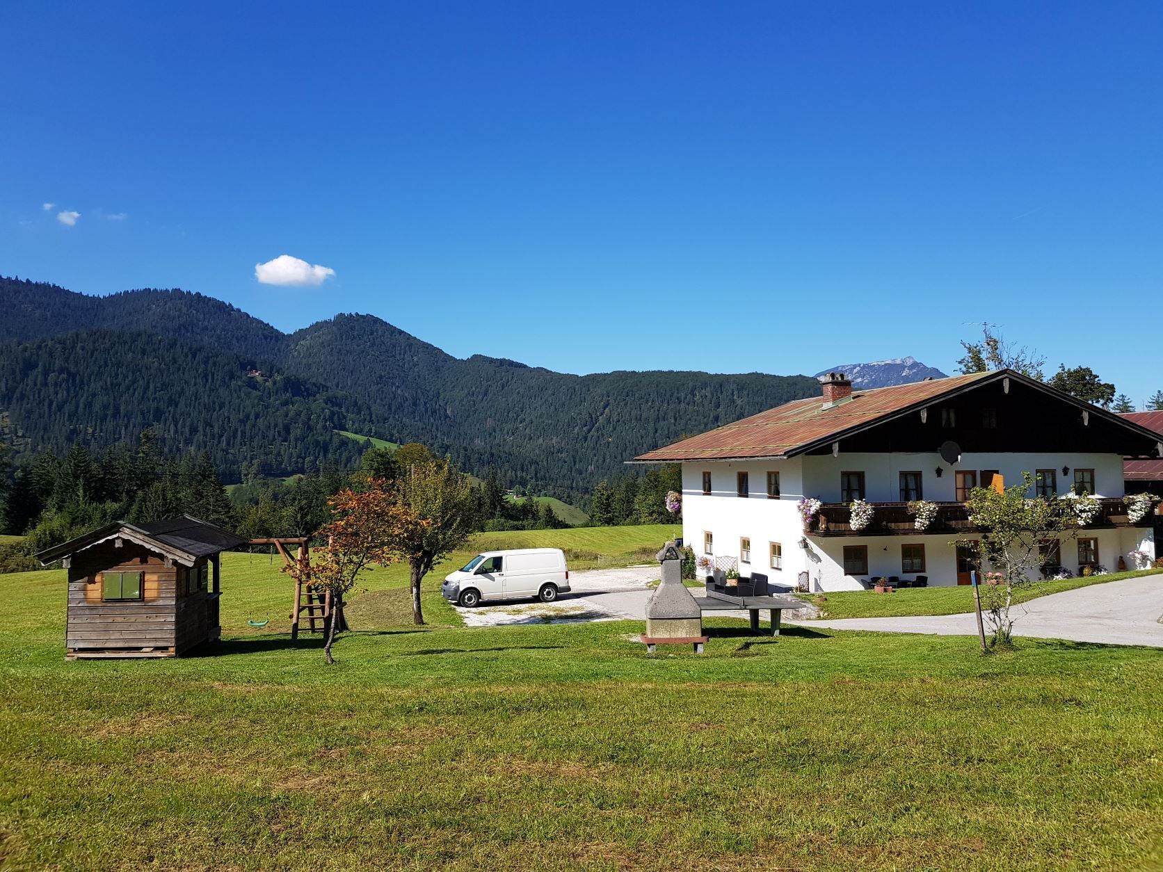 A rural setting with a large white building, a small wooden structure, and a white van.
