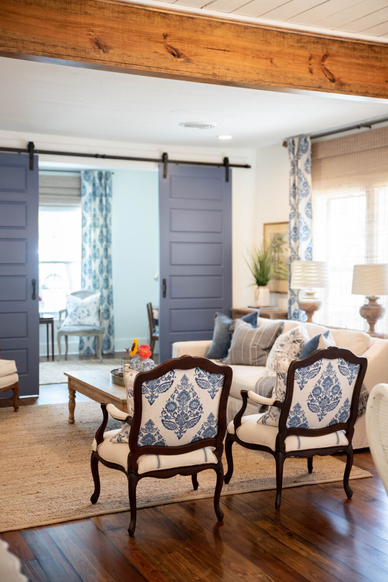 Een woonkamer met een houten plafond, een bank, twee gestreepte fauteuils, een salontafel en een schuifdeur.
