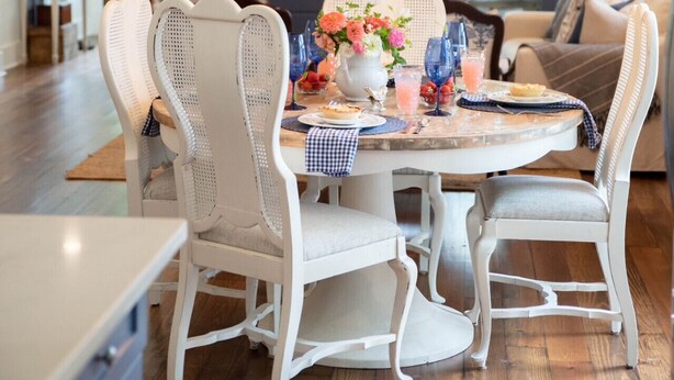 A dining area with white wicker chairs, a round table, and a chandelier. - Charming Historic District Cottage Near Downtown (Conway)