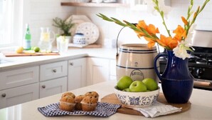 A kitchen counter with a blue vase, a bowl of green apples, and muffins on a checkered cloth. - Charming Historic District Cottage Near Downtown (Conway)