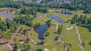 Ilmakuva golfkentästä, jossa on useita lampia, vihreitä väyläalueita ja hiekkabunkkereita.