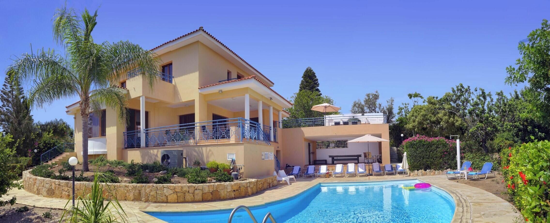 A two-story building with a swimming pool, lounge chairs, and a covered area with umbrellas.