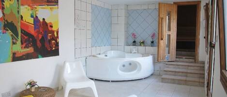 A bathroom with a freestanding bathtub, white chairs, and a colorful abstract painting.