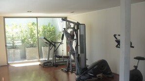 Une pièce spacieuse dotée d’une grande porte-fenêtre coulissante donnant sur un espace extérieur, ainsi que d’un vélo d’appartement et d’un appareil de musculation.