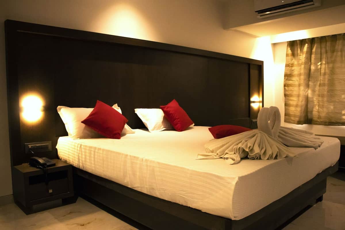 Una habitación de hotel con una cama grande, lámparas de noche, un teléfono y un ventanal con cortinas.