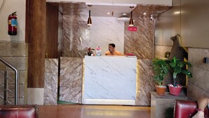 Zona de recepción de un hotel con un mostrador de mármol, un extintor en la pared, un pilar de madera y un recepcionista.