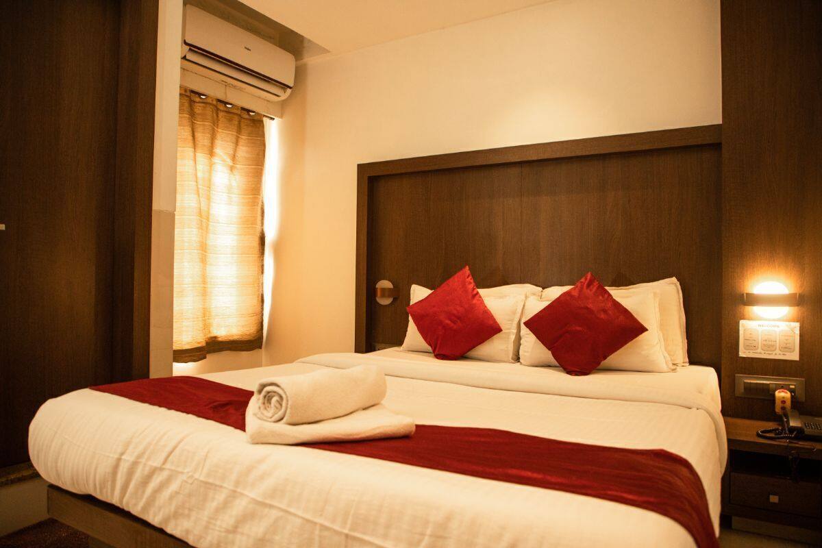 Una habitación de hotel con una cama, una manta roja y una almohada blanca.