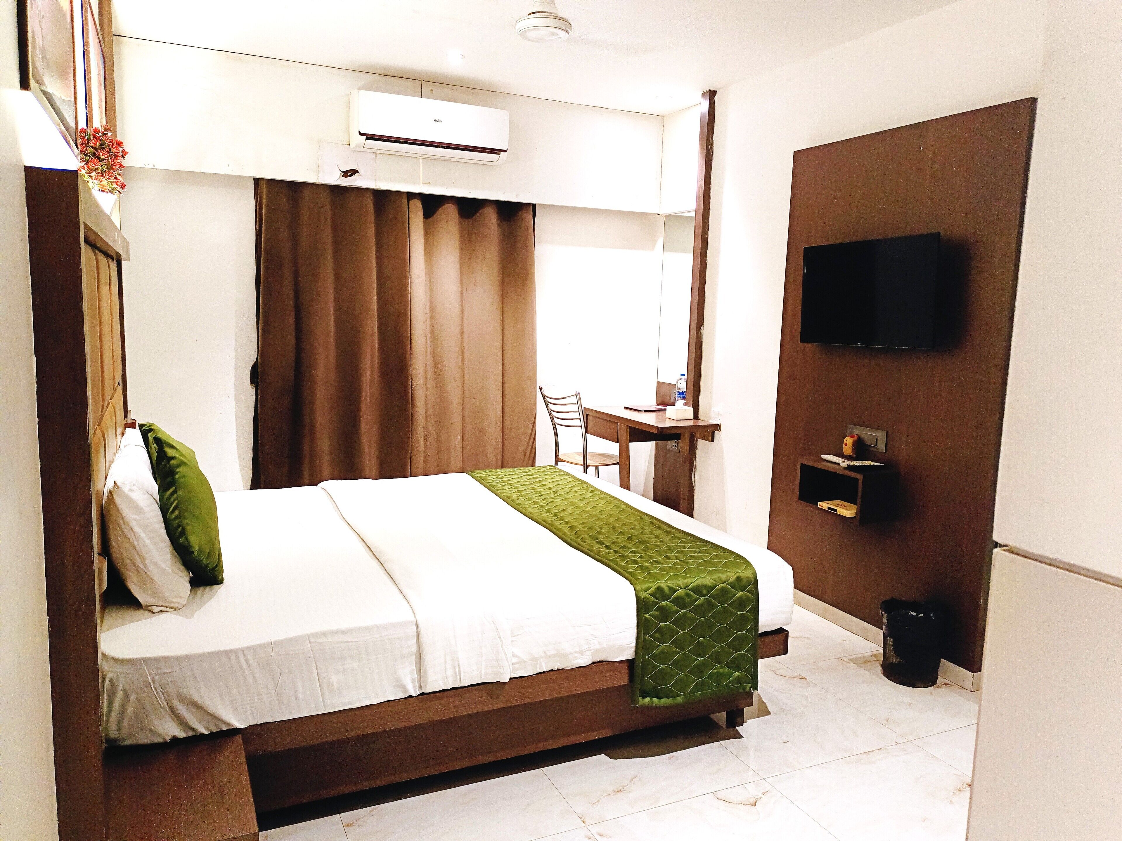 Une chambre d’hôtel équipée d’un lit, d’un bureau, d’une chaise, d’un climatiseur, d’une télévision et d’une poubelle.