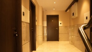 Un pasillo de hotel con suelo de mármol, una puerta de madera y una barandilla de metal.