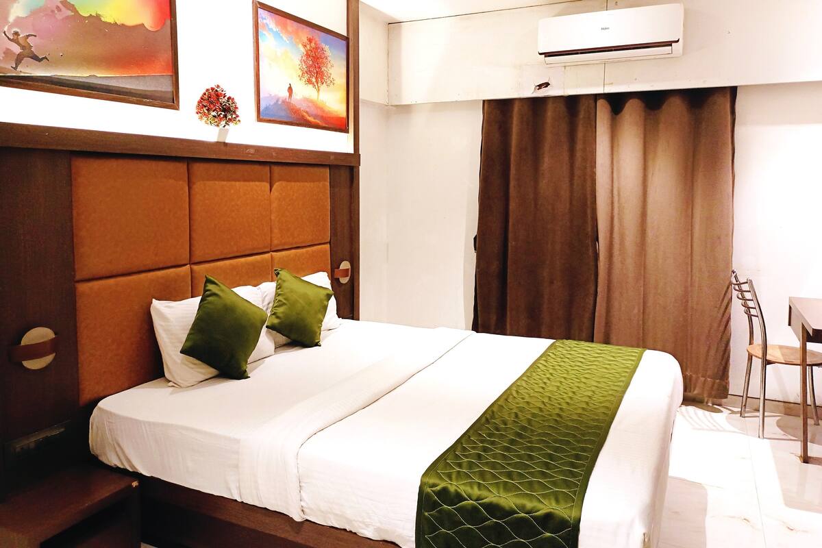 Habitación de hotel con cama, cabecera, un cuadro, unidad de aire acondicionado y cortina.