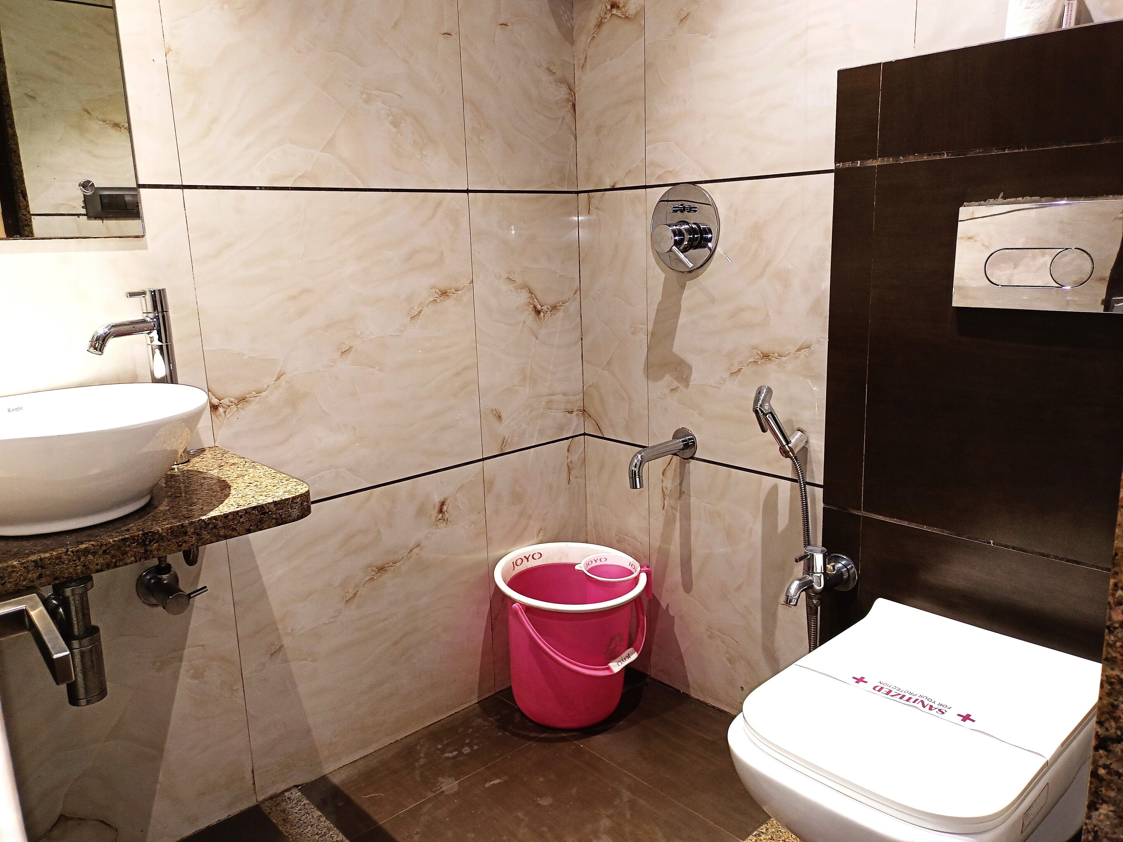 A bathroom with a white sink, a toilet, and a shower. There is a pink bucket on the floor.