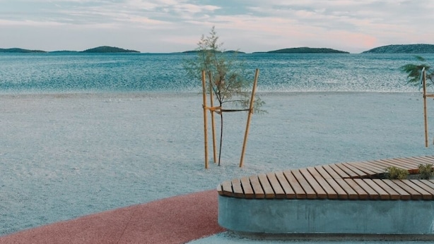 Une promenade en bord de mer qui mène à une terrasse en bois offrant une vue sur la mer et les îles lointaines.