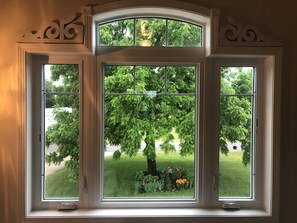 A large arched window with three panes, offering a view of a lush garden and a tree. - Newer, spacious and clean cottage with river view! (Harpers Ferry)