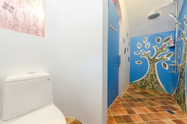 A bathroom with a toilet, a shower with a tree mural, and tiled flooring.