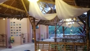 An outdoor dining area with wooden tables and chairs, a thatched roof, and a view of the street. - Red Forest Guest House (Coron)
