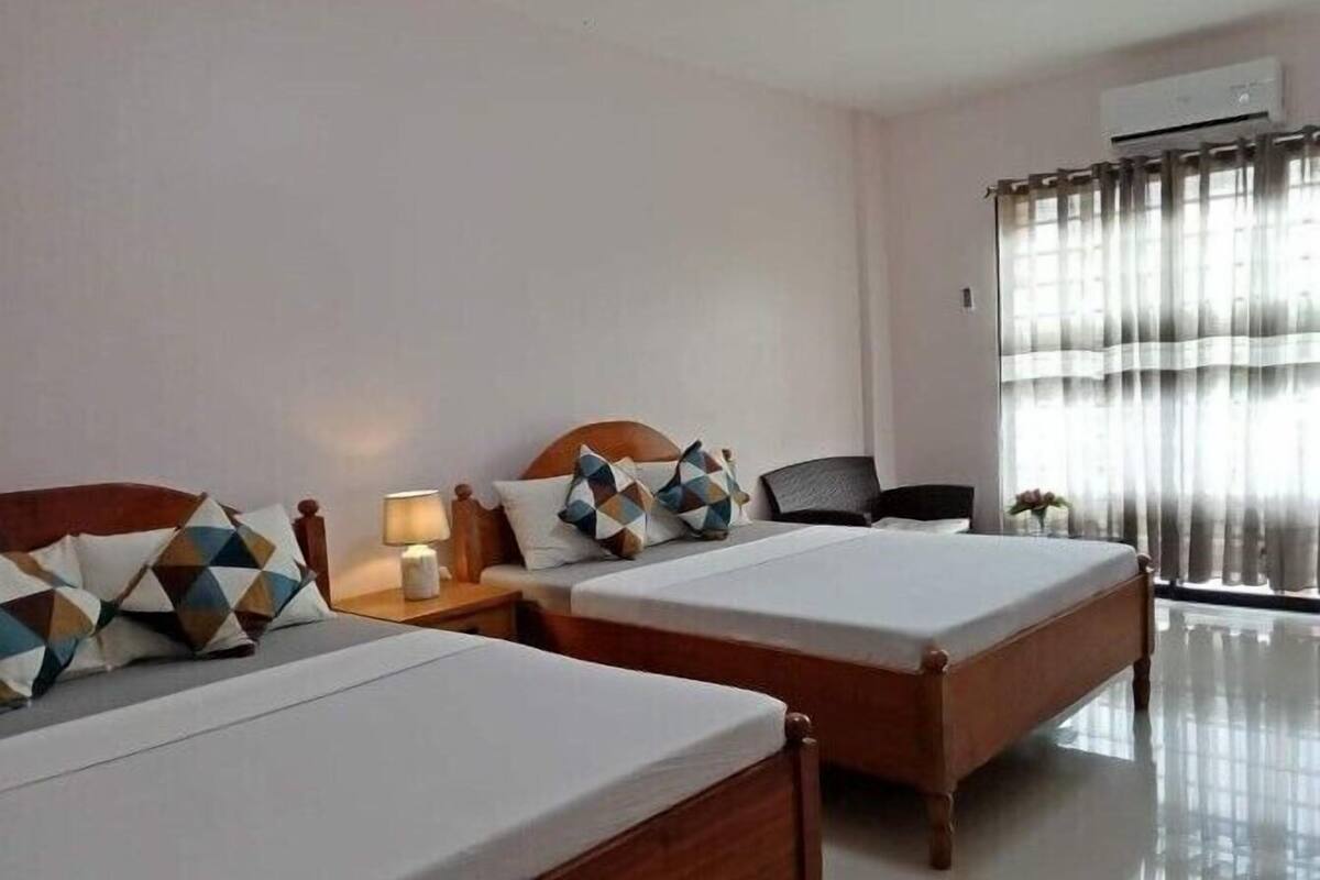 A hotel room with two beds, a desk, a chair, and a window with curtains.