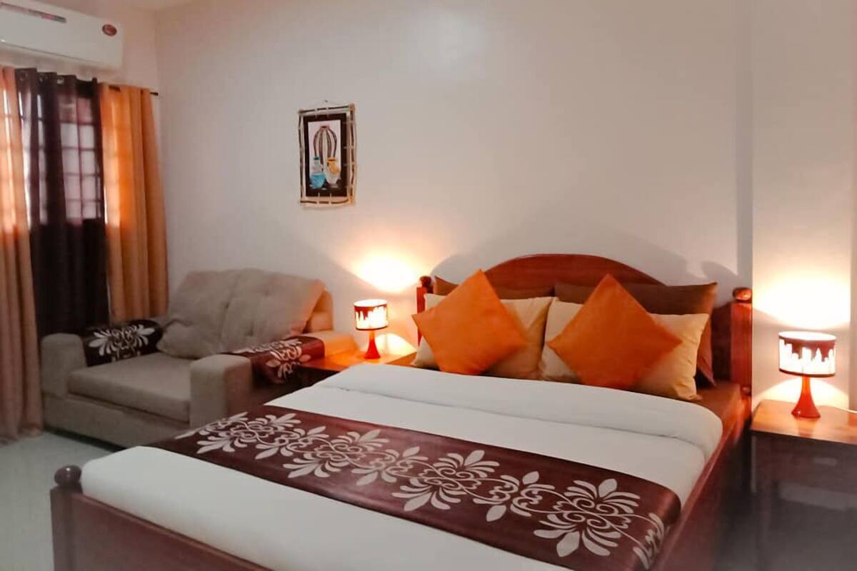 A hotel room with a bed, a chair, two bedside lamps, and a picture on the wall.