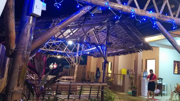 A rustic wooden structure with a thatched roof, decorated with blue string lights. - Red Forest Guest House (Coron)