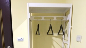 Una estantería blanca con tres repisas y ganchos para colgar objetos, ubicada frente a una pared amarilla con una puerta a la izquierda.