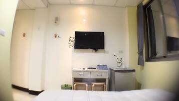 Una habitación de hotel con una cama, un escritorio con silla, una mesita, un cubo de basura y un televisor montado en la pared.
