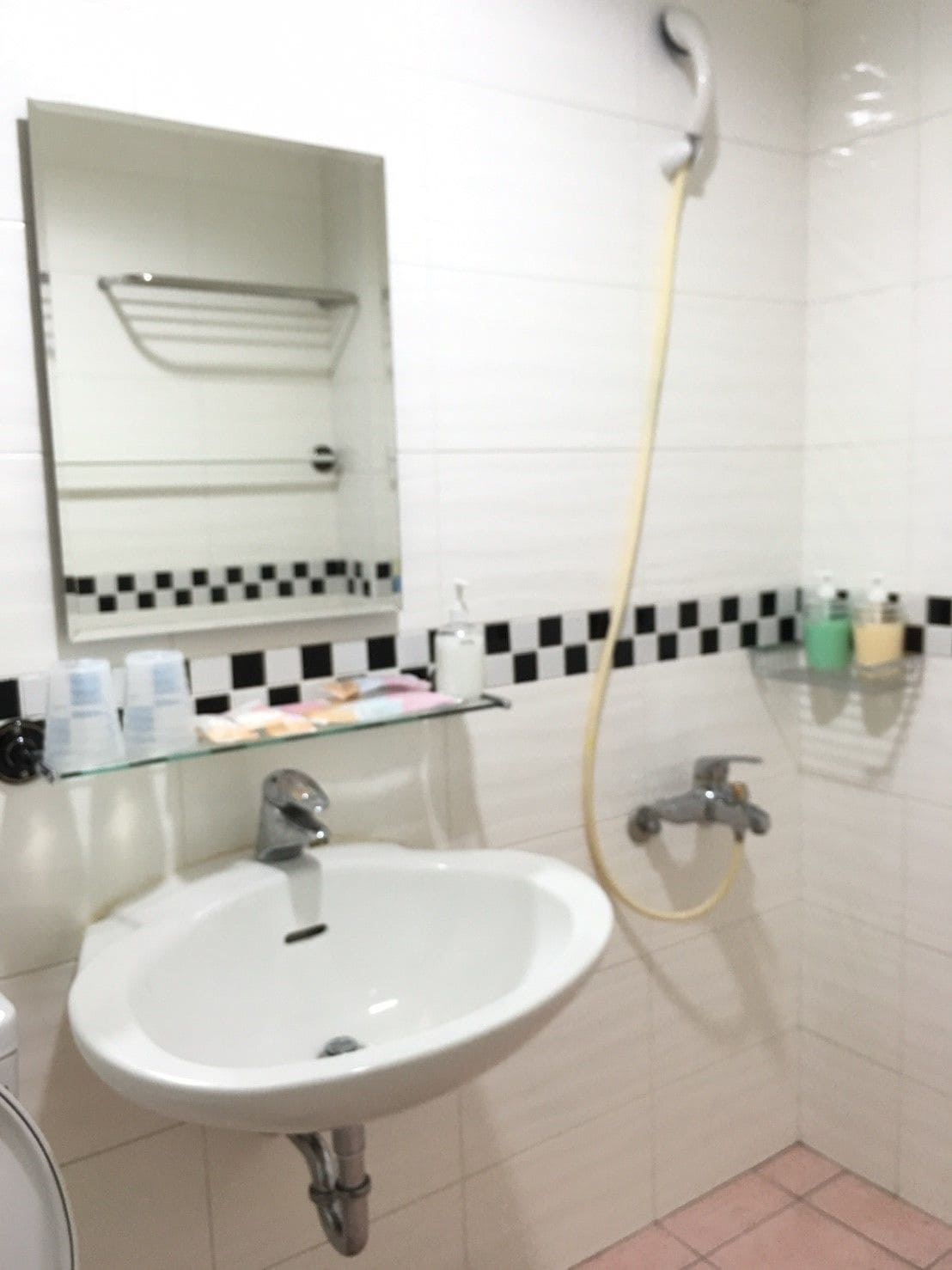 A bathroom with a white sink, a mirror above it, and a shower with a yellow hose.