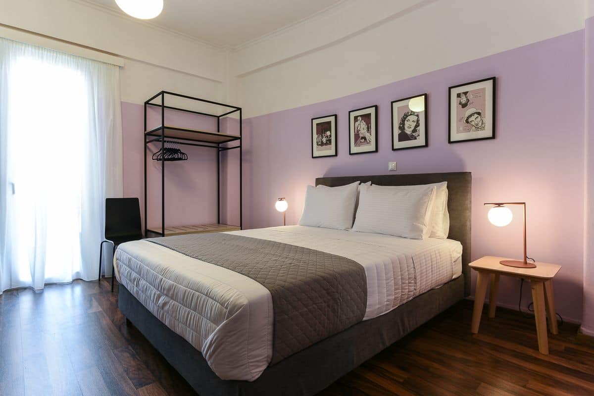 A bedroom with a bed, a bedside table with a lamp, a wall-mounted shelf, and framed pictures.