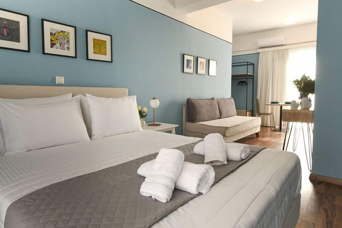 A hotel room with a large bed, a sofa, a desk, and a view of the outdoors.