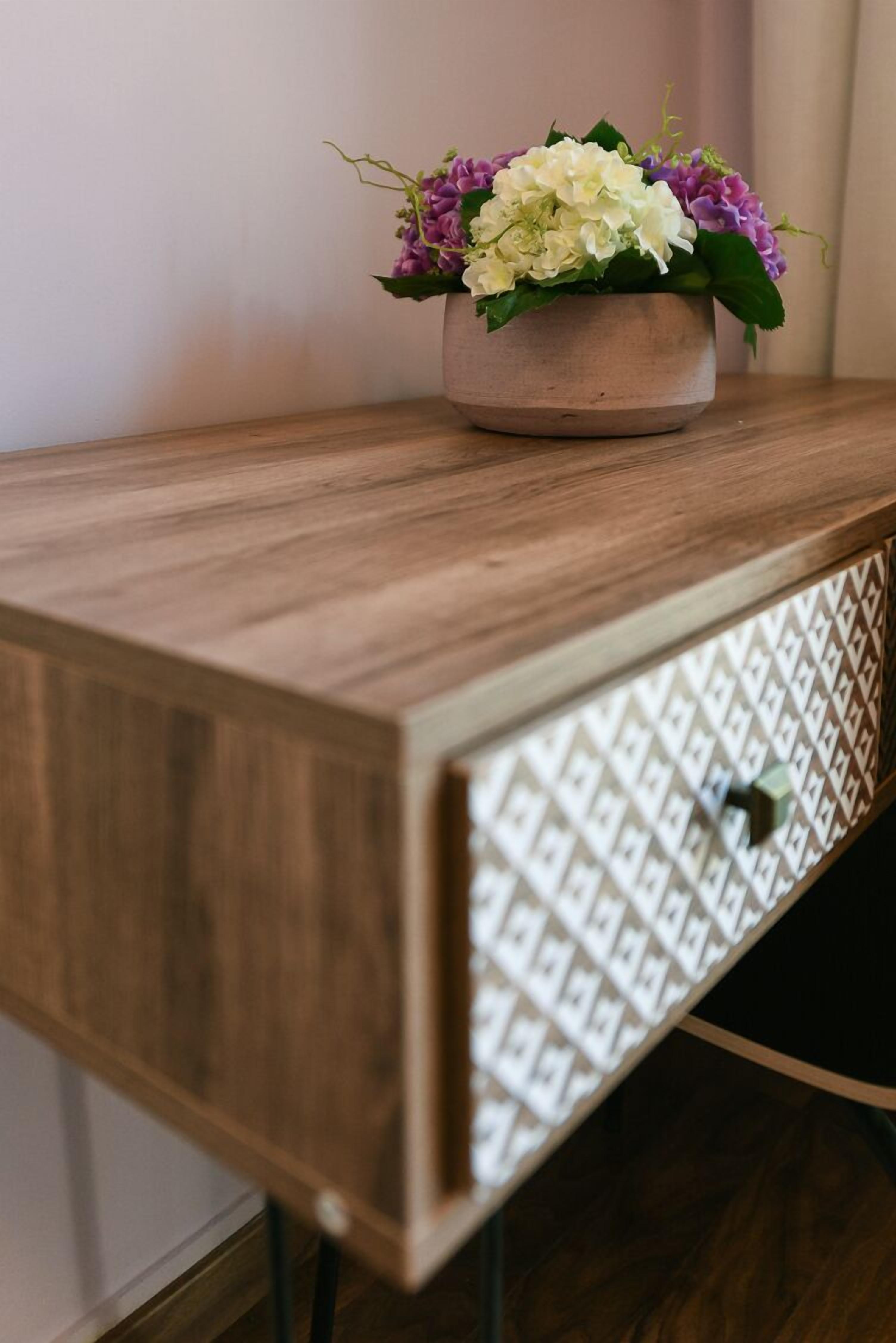 Una consola de madera con un jarrón decorativo lleno de flores.