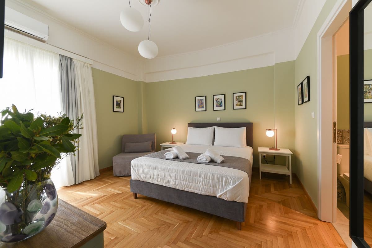 A bedroom with a bed, bedside tables, a nightstand, a potted plant, and a window with curtains.