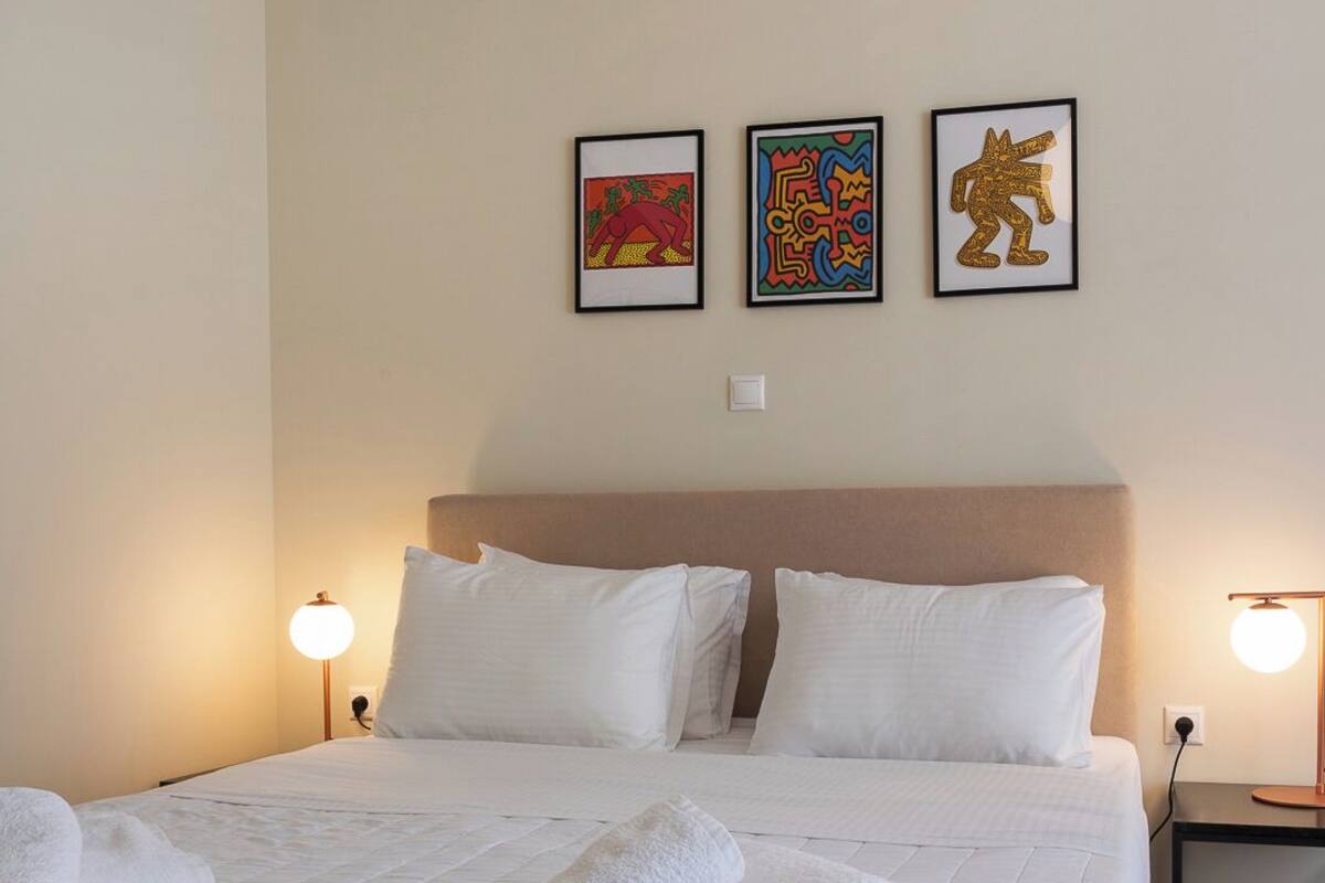 A neatly made bed with white linens and two towels, a headboard, and three framed artworks on the wall.