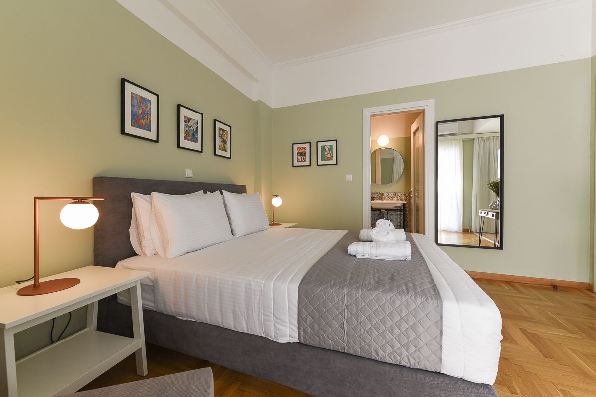 Un dormitorio ordenado con cama, mesitas de noche, un espejo y cuadros en la pared.